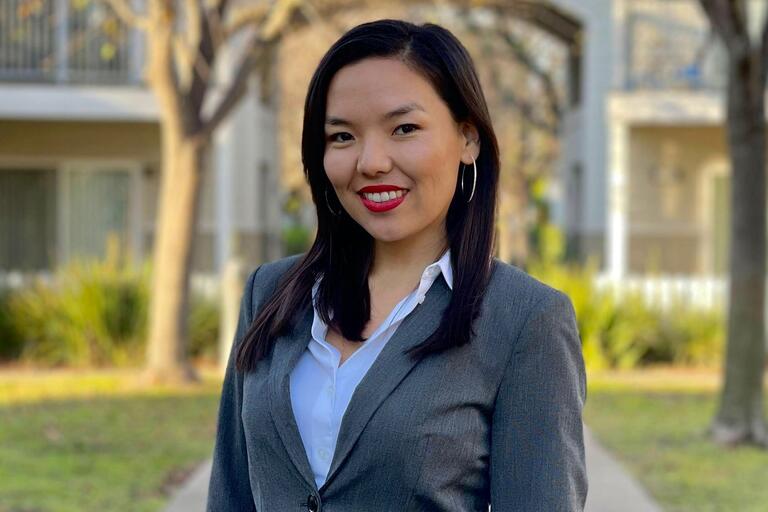 Young smiling woman with dark medium lengh hair, red lipstick, white blouse, gray jacket