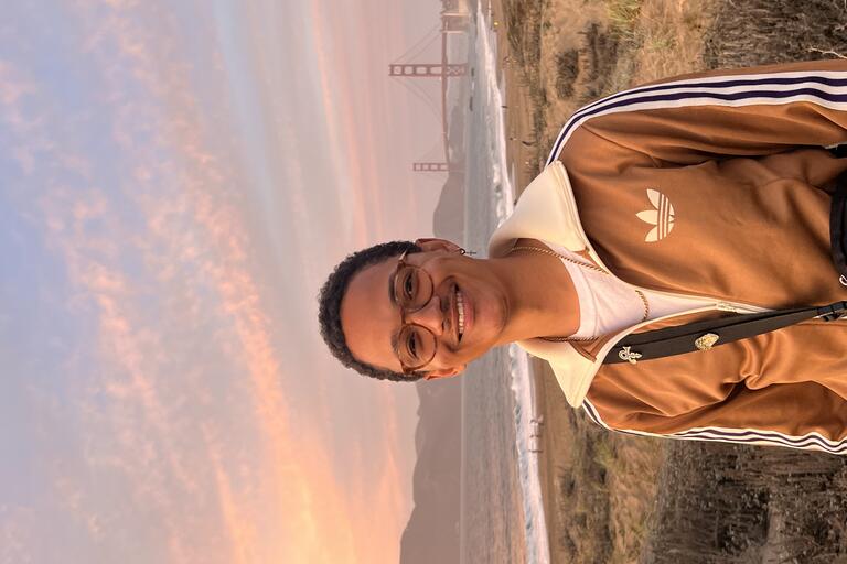 Young smiling man wearing white tshirt gold Addidas jacket, background of beach and Golden Gate Bridge